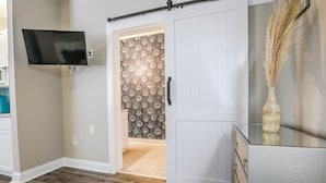 A room with a sliding door leading to a bathroom, a mounted TV, and a decorative vase. - My Vitamin Sea Quaint Studio Myrtle Beach SC (Myrtle Beach)