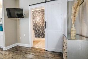 A room with a sliding door leading to a bathroom, a mounted TV, and a decorative vase. - My Vitamin Sea Quaint Studio Myrtle Beach SC (Myrtle Beach)