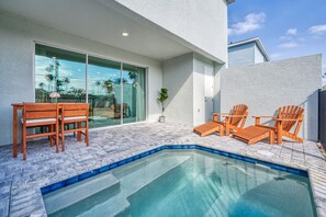 A modern outdoor pool area with a glass-enclosed patio, wooden chairs, and a small table. - Affordable Luxury Home for 8 Guests Close to Parks (Kissimmee)