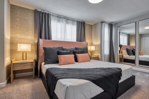 Una habitación de hotel moderna con una cama grande, dos mesitas de noche con lámparas, un espejo amplio y suelo alfombrado.
