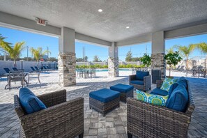 A covered outdoor seating area with wicker furniture and a pool in the background. - Affordable Luxury Home for 8 Guests Close to Parks (Kissimmee)