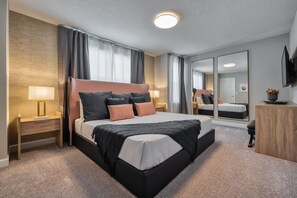 A modern hotel room with a large bed, a bedside table with a lamp, a wooden nightstand, a mirror, and a TV mounted on the wall. - Affordable Luxury Home for 8 Guests Close to Parks (Kissimmee)
