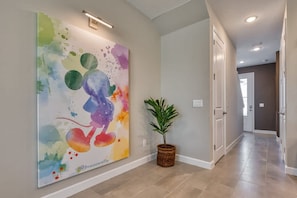 Un couloir orné d’un grand tableau abstrait, d’une plante en pot et d’une porte au fond.