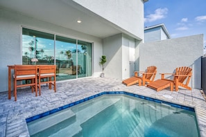 A swimming pool with wooden chairs and a table, surrounded by a paved patio. - New Modern Villa With Pool 5 Minutes From Disney (Kissimmee)