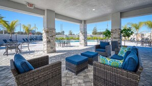 A covered outdoor seating area with wicker furniture and a pool in the background. - Luxury Modern Villa With Private Pool 10 min From Disney (Kissimmee)