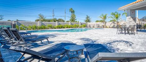 A poolside area with lounge chairs, a small round table, and a covered seating area.