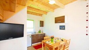 Cocina compacta con techo de madera, una mesa de comedor con sillas y un televisor montado en la pared.