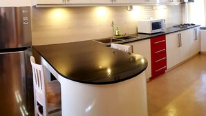 A kitchen with a stainless steel refrigerator, a microwave, and a stove. There is a white chair and a red cabinet. - Myhavelock Town Studio Apt, With Own Pvt Gate Parking in Main City (Colombo)