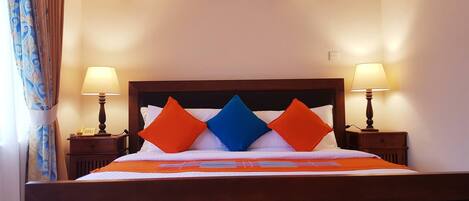 Quarto de hotel com cama, duas luminárias de cabeceira, ar condicionado fixado na parede e uma tomada.