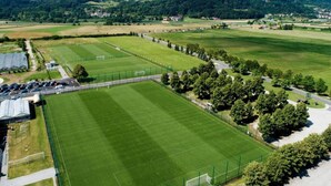 Een groot, rechthoekig sportveld met een hek, omringd door bomen en gebouwen.