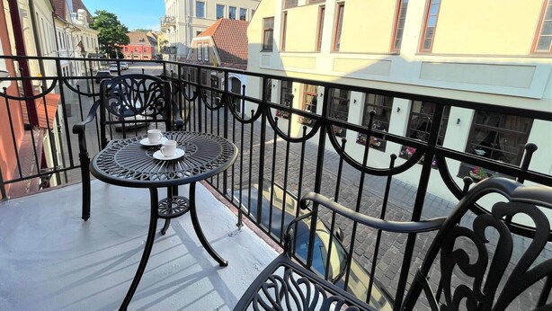 A balcony with a round metal table and chairs, overlooking a street with buildings and a clear sky. - Picturesque Old Town Apartment With Balcony (Kaunas)