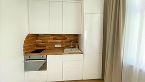 A compact kitchen with white cabinetry, a wooden backsplash, a built-in dishwasher, and a refrigerator. - Picturesque Old Town Apartment With Balcony (Kaunas)