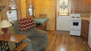 A cozy cabin interior with wooden walls, a dining table, a sofa, a lamp, a stove, and wooden cabinets.