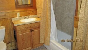 A bathroom with a wooden vanity, a sink, a mirror, and a shower area.