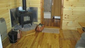 A wooden cabin interior with a wood-burning stove, a door leading to a bathroom, and a small rug on the floor.