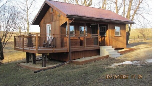 A wooden cabin with a porch, a small deck, and a metal roof.