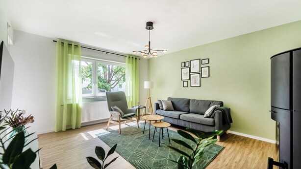 A modern living room with a sofa, a chair, a small table, and a green patterned rug. - City-Luxury Apartment Rottweil (Rottweil)