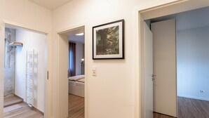 A hallway with a wooden floor, a framed picture on the wall, and a door leading to a bedroom with a bed. - City-Luxury Apartment Rottweil (Rottweil)