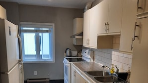 Cocina compacta con armarios blancos, horno integrado, un lavabo y un ventanal que proporciona luz natural.