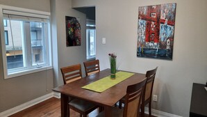 Un comedor con una mesa de madera, cuatro sillas, un jarrón de flores y dos cuadros en las paredes.