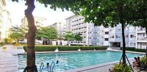 A swimming pool surrounded by a landscaped area with trees and a multi-story building in the background. - Discover Your Home Away From Home- Unwind in Our Exquisite Retreat! (Caloocan)
