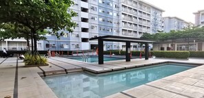 A swimming pool with a covered area, surrounded by a building with multiple balconies and air conditioning units. - Discover Your Home Away From Home- Unwind in Our Exquisite Retreat! (Caloocan)