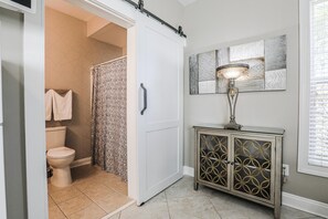 A bathroom with a toilet, shower curtain, and cabinet with decorative glass doors. - Modern Gray Studio Steps to Pool Myrtle Beach SC (Myrtle Beach)