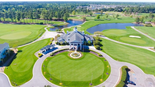 Un parcours de golf doté d’un club-house, d’un étang et d’une zone résidentielle en arrière-plan.