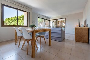 A modern dining area with a wooden table and chairs, a sofa, and a wicker cabinet.