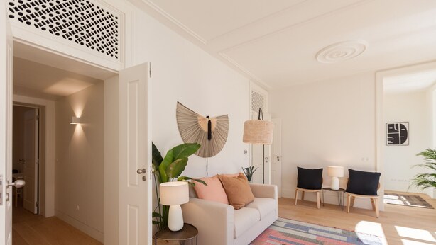 Een moderne woonkamer met een witte bank, twee fauteuils, een kamerkleed met dessin en een grote plant.