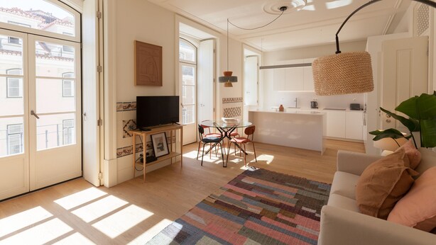 A bright living room with a TV, a dining table, and chairs. There is a kitchen area in the background. - FLH Downtown Central Boho Flat (Lisboa ciudad)