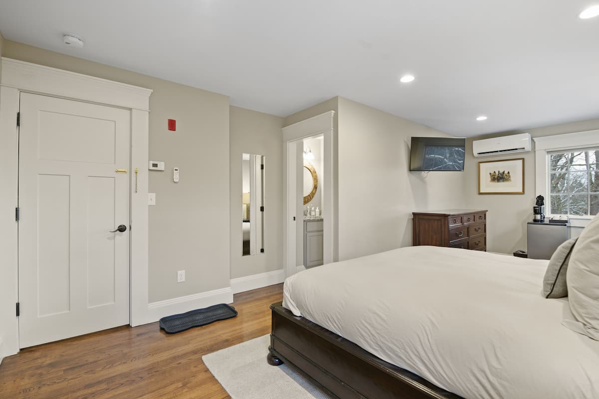 A bedroom with a large bed, a dresser, a vanity, and a television mounted on the wall.