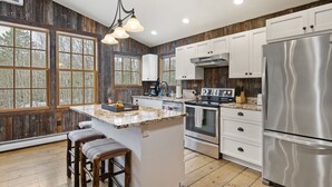 Une cuisine moderne avec des éléments en bois, un grand îlot central, des appareils en acier inoxydable et une vue sur l’extérieur.