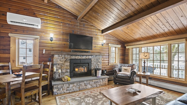 L’intérieur d’une cabane en rondins, avec une cheminée en pierre, des meubles en bois et de grandes fenêtres.