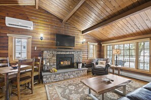 A log cabin interior with a stone fireplace, wooden furniture, and large windows. - Brook Bound Inn (Wilmington)