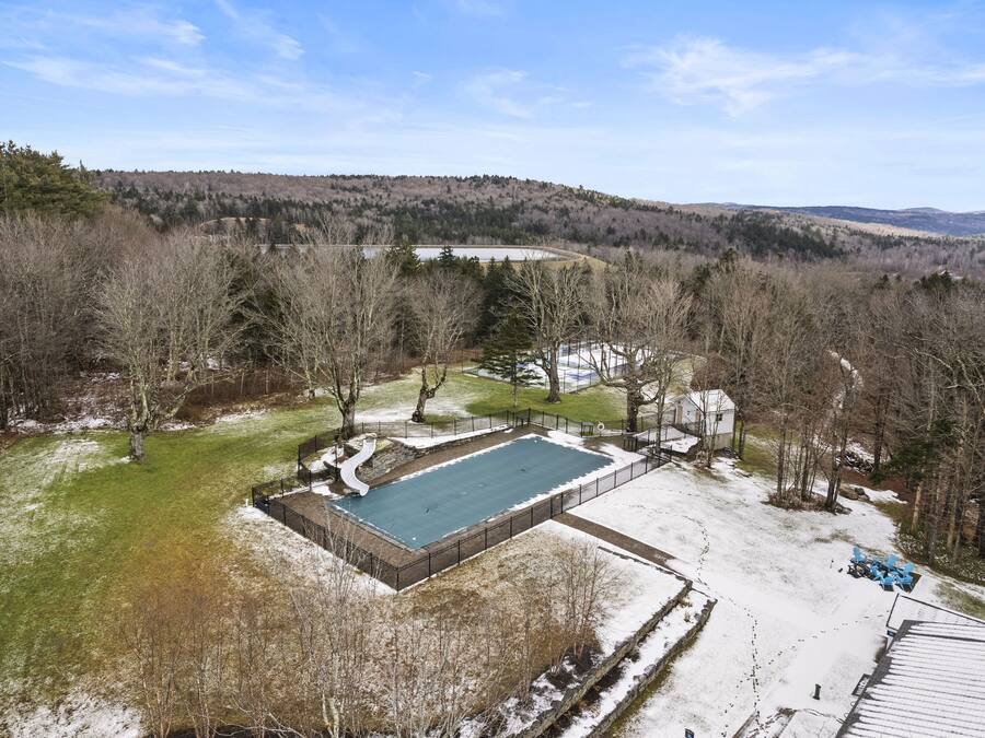 A large rectangular swimming pool surrounded by a fence, with a grassy area and trees nearby.