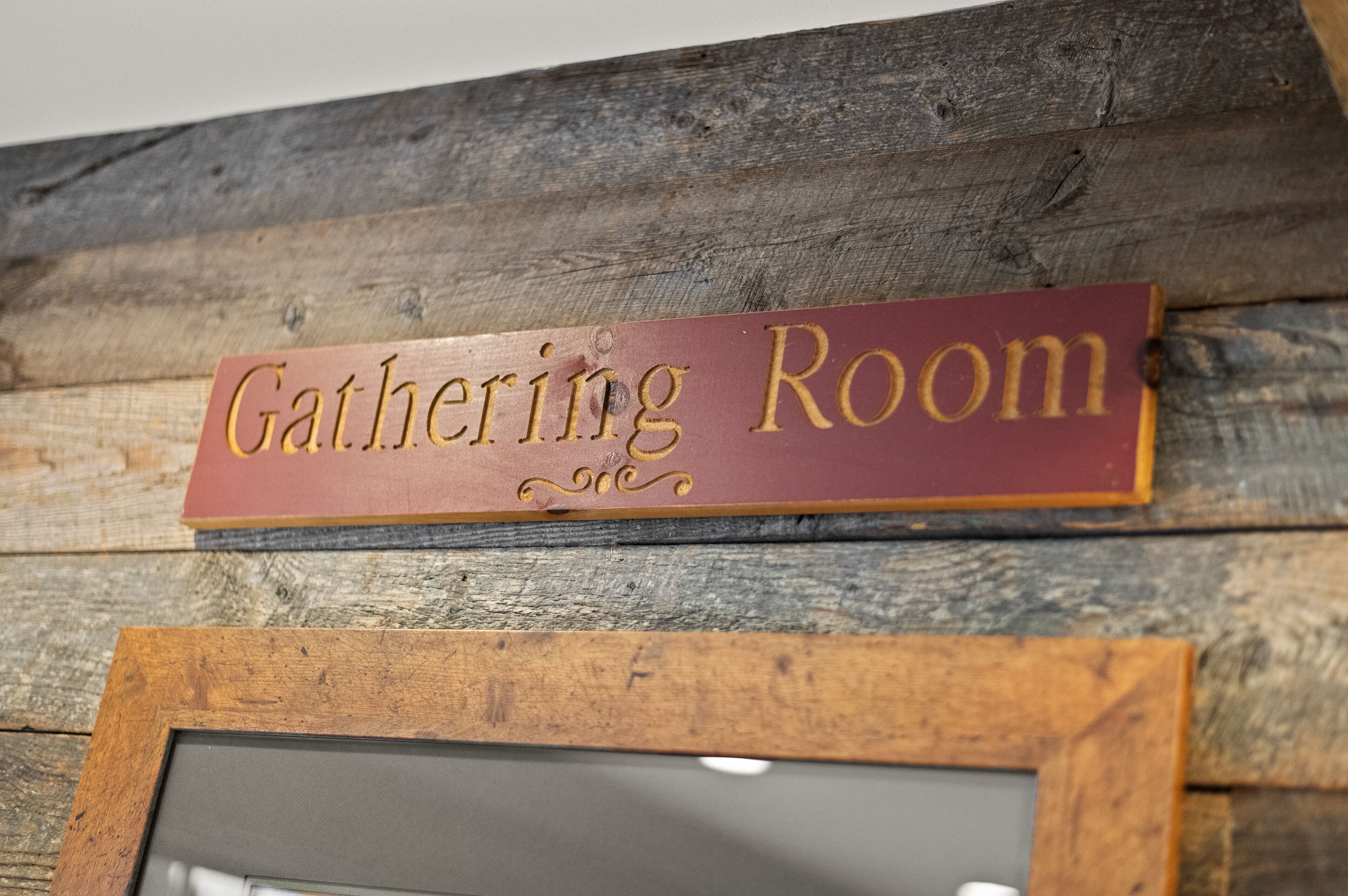 A sign labeled "Gathering Room" on a rustic wooden wall.