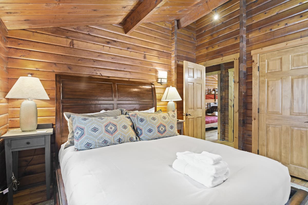 A wooden cabin-style bedroom with a large bed, two bedside lamps, and a wooden door.