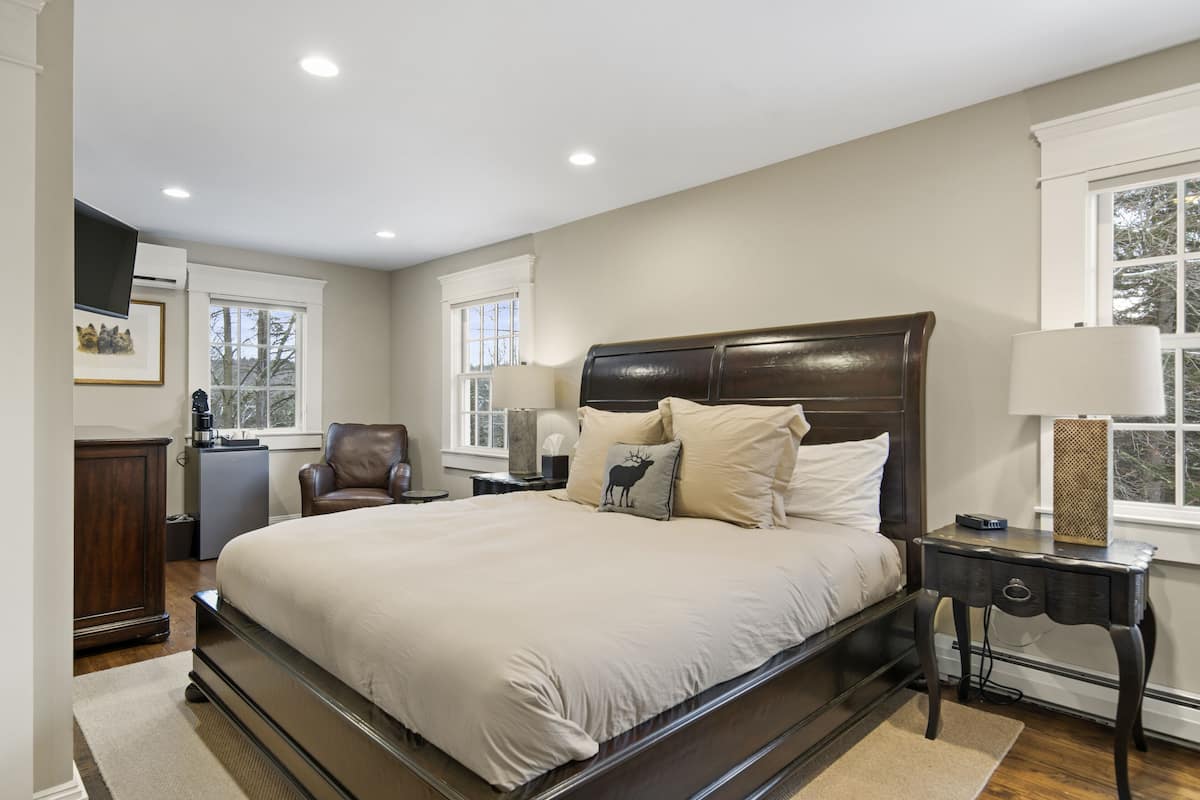 A bedroom with a large bed, a dresser, a chair, and a nightstand with a lamp.