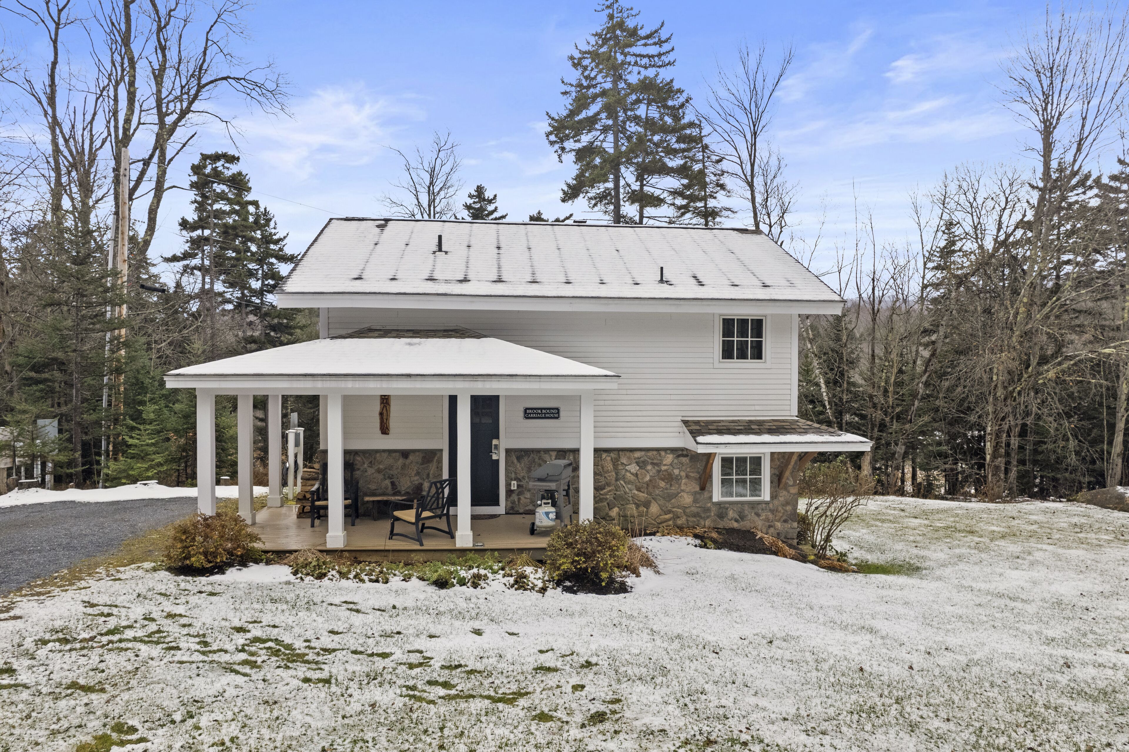 A two-story house with a covered porch, stone foundation, and a small attached garage.