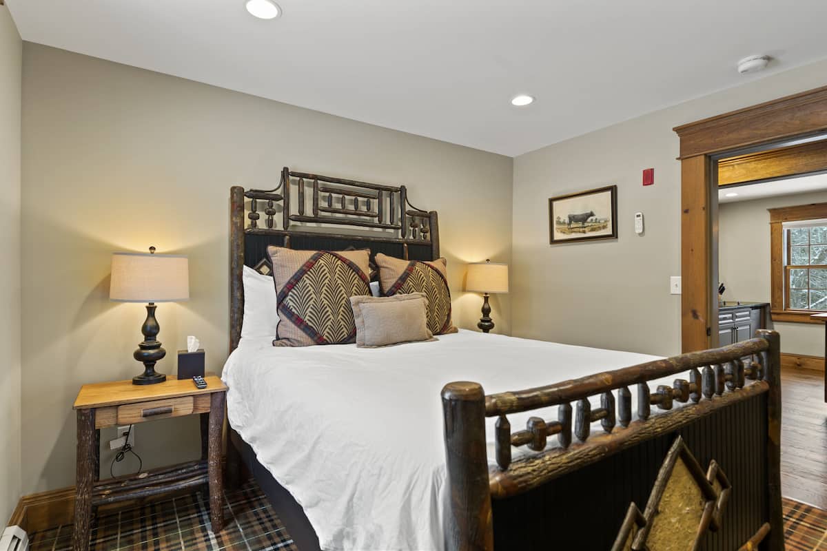 A neatly arranged bedroom with a large bed, two bedside tables with lamps, a wooden headboard, and a framed picture on the wall.
