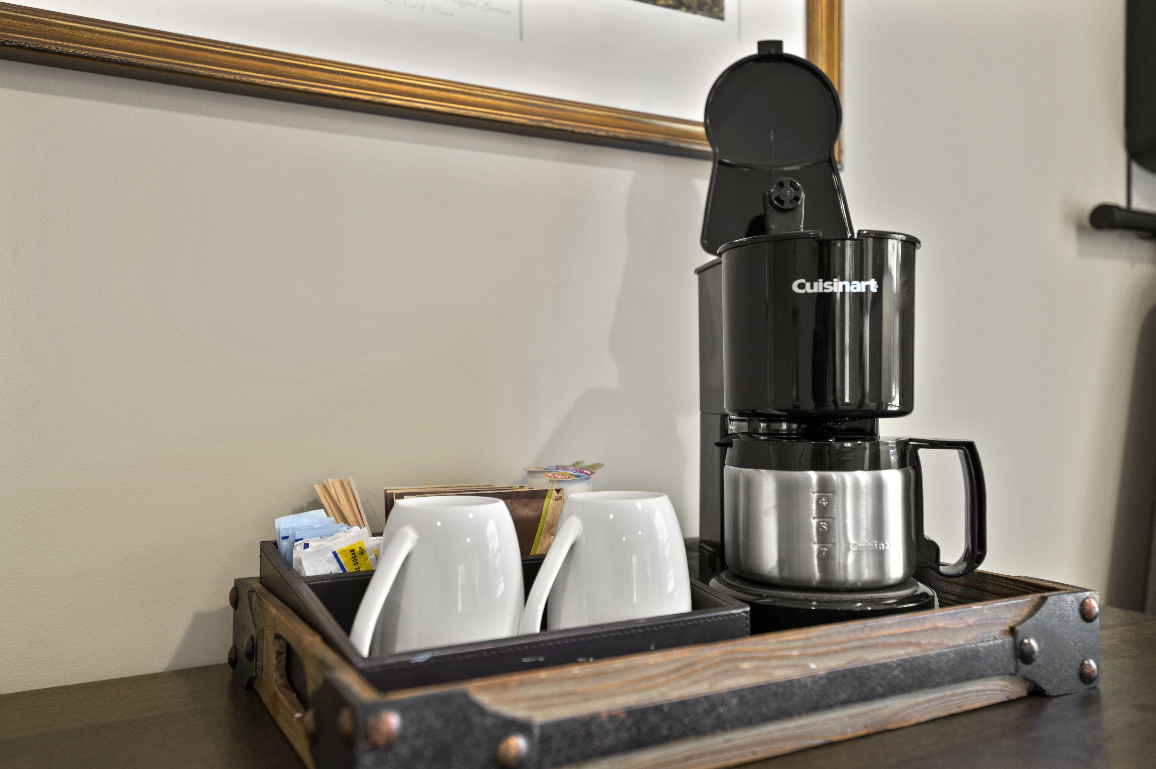 A Cuisinart espresso machine on a wooden tray with white cups and a box of coffee pods.