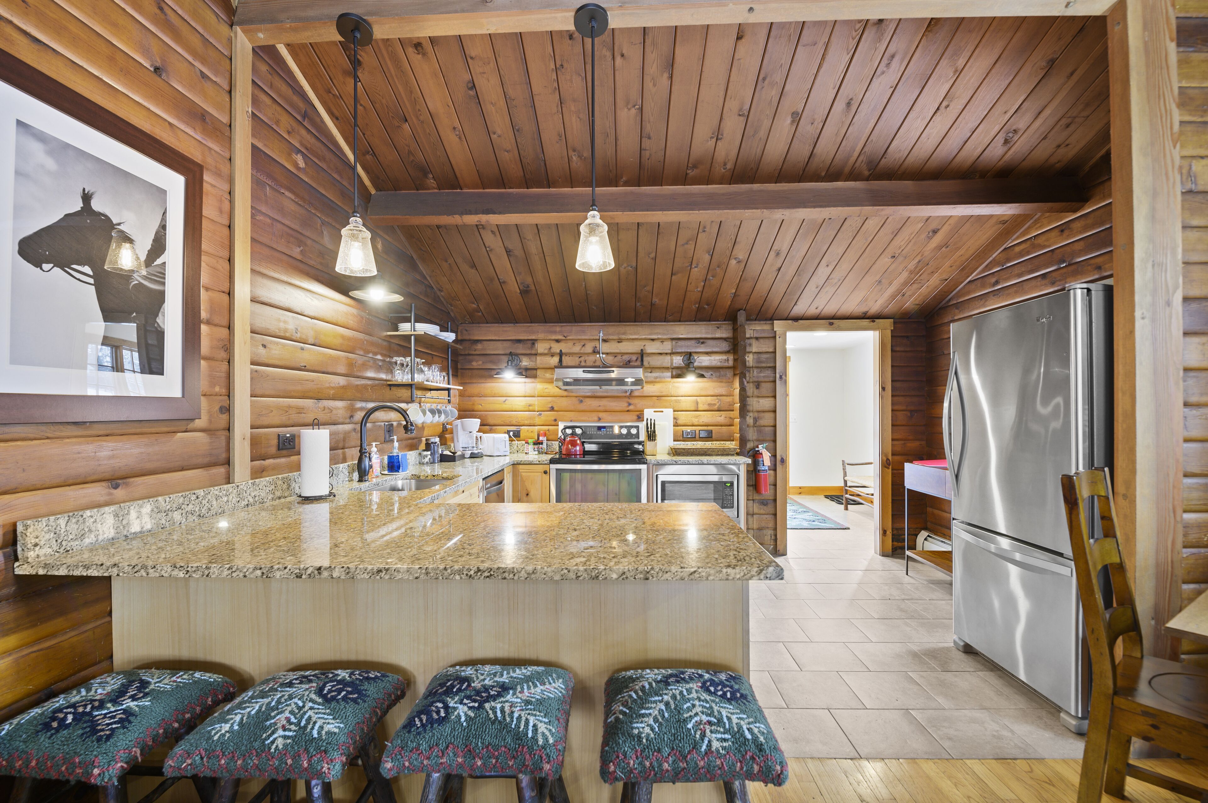 Una cocina con paredes de madera, encimera de granito y refrigerador de acero inoxidable.