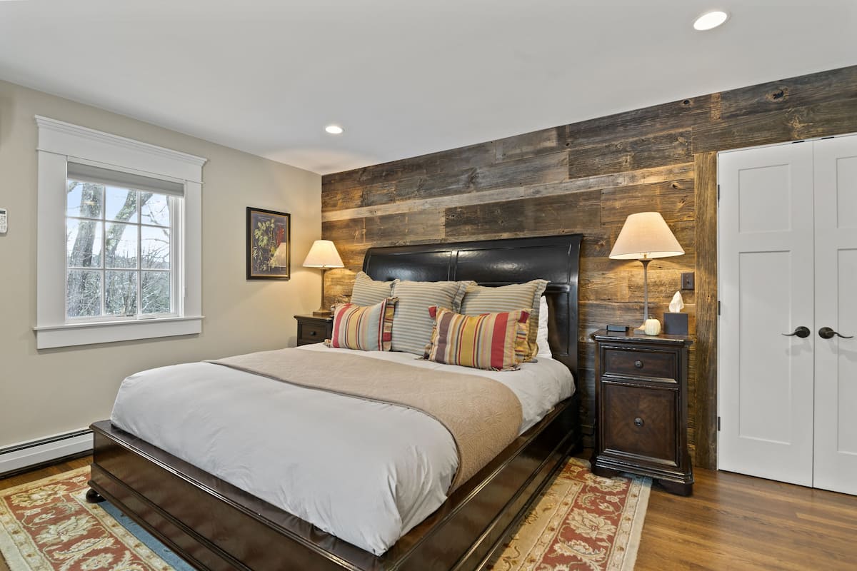 A bedroom with a large bed, wooden headboard, two bedside tables with lamps, a window, and a door.