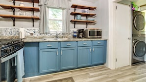 Een keuken met blauwe kastjes, een fornuis, een magnetron en een wasmachine.