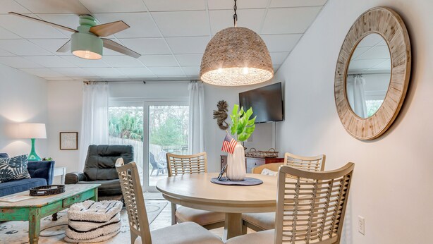 A dining area with a round table, chairs, a ceiling fan, and a large mirror on the wall. - Chic Gulf Breeze Escape w/ Pool Access & Courtyard (Gulf Breeze)