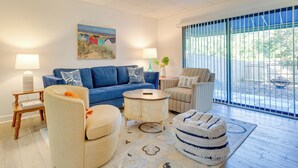 A living room with a blue sofa, beige armchairs, a round coffee table, and a patterned rug. - Chic Gulf Breeze Escape w/ Pool Access & Courtyard (Gulf Breeze)