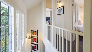 A staircase with white railings and a handrail, leading to a bedroom with a bed and a nightstand. - 4 Bed - Beach Cottage (Torquay)