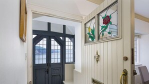 A hallway with a dark blue door, a white bench, and a stained glass window with a rose design. - 4 Bed - Beach Cottage (Torquay)