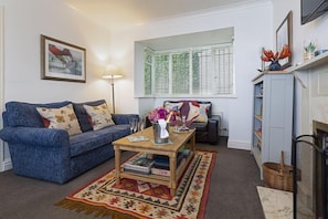 Een woonkamer met een blauwe bank, een houten bijzettafeltje en een vloerkleed met een patroon.